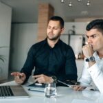 Two men in office attire focused on laptop, discussing business strategies.
